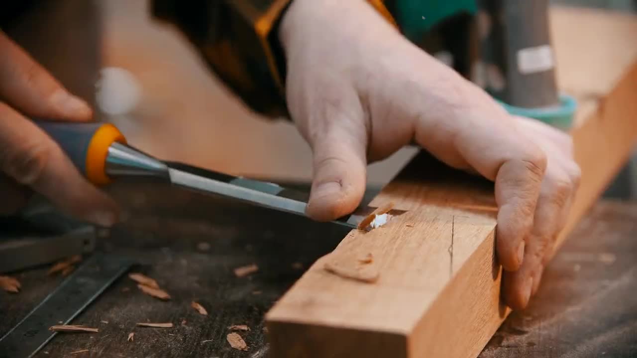 Hände stemmen mit einem Stemmeisen ein Zapfenloch in ein Holzstück