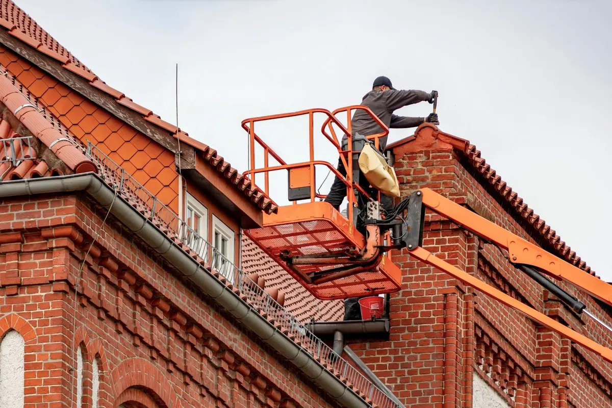 Dachdecker auf einer Hebebühne arbeitet am Dach eines alten Backsteinhauses