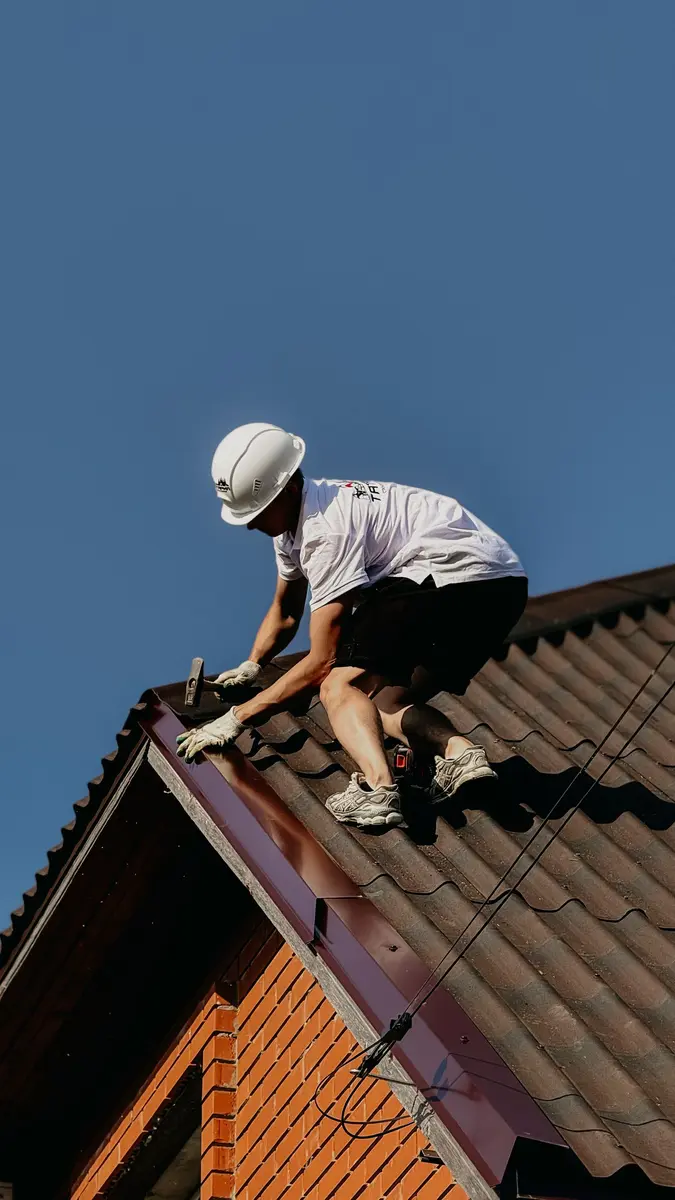 Dachdecker mit Helm arbeitet auf einem Dach unter blauem Himmel