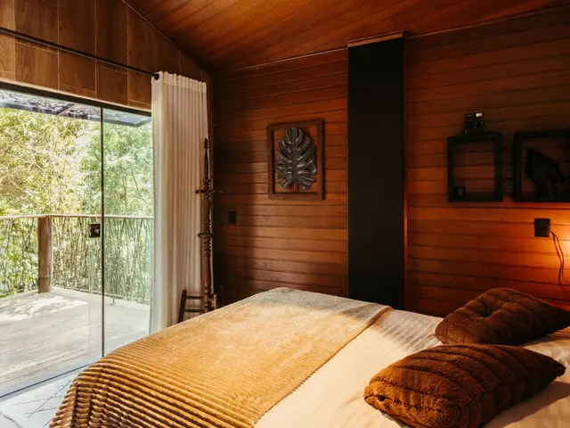 Doppelzimmer mit Holzwänden, Bett mit warmen Decken und Glastür zum Balkon